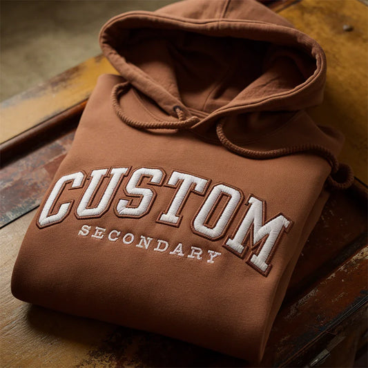 Brown hoodie with 'CUSTOM SECONDARY' text on a wooden surface